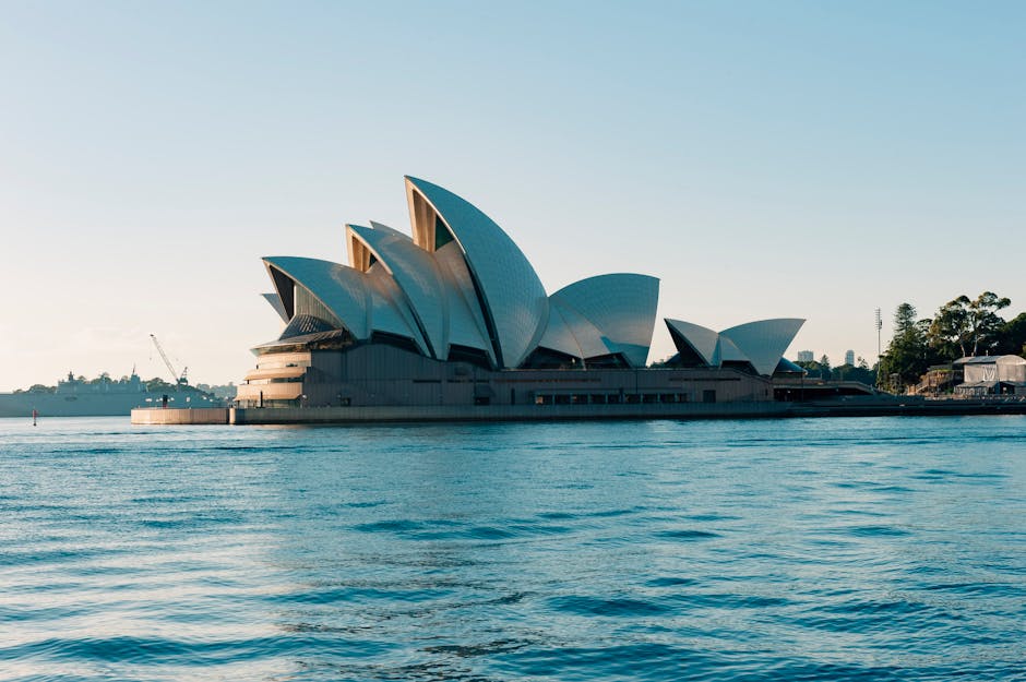 Scenic view of the iconic Sydney Opera House against a clear morning sky with calm water reflections.
