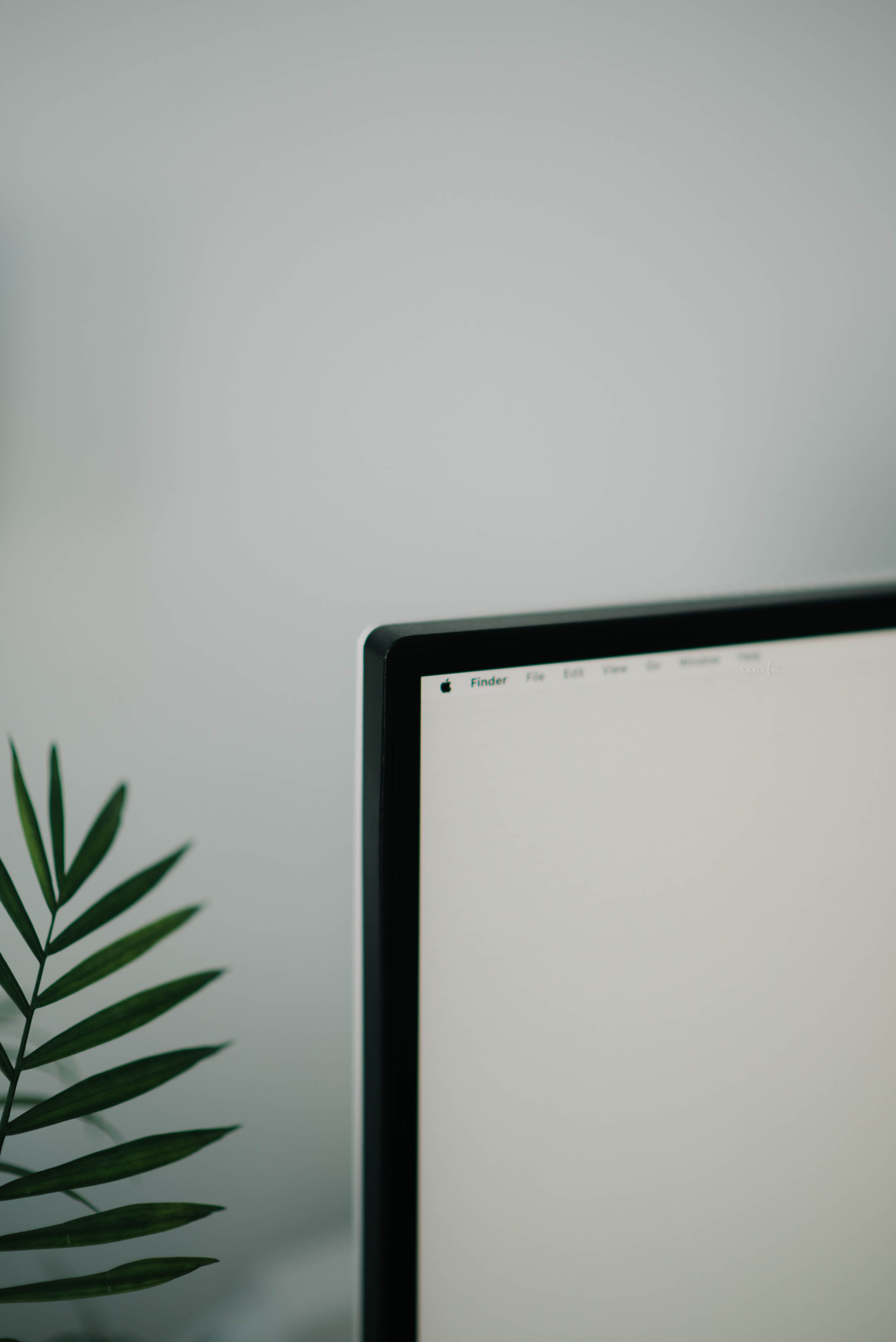 A minimalist workspace featuring a monitor, a small plant, and a desk lamp, representing a controlled environment that reduces cognitive load and promotes focus.