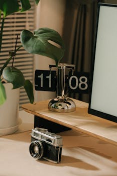 A stylish desk setup featuring a vintage camera, flip clock, and potted plant.