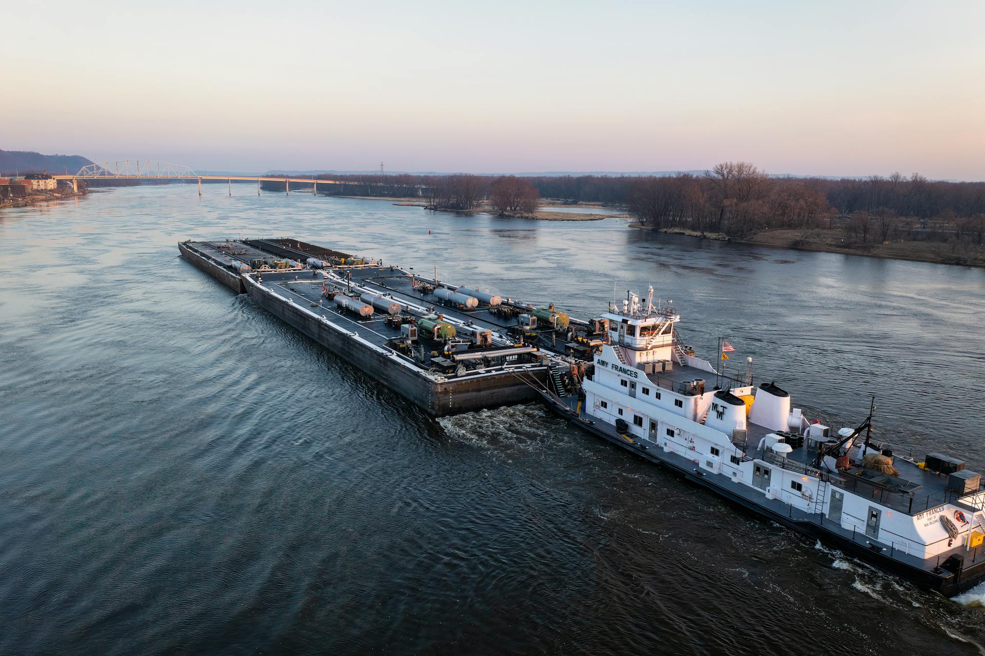 A cargo barge navigating the Mississippi River in Wabasha at sunset.