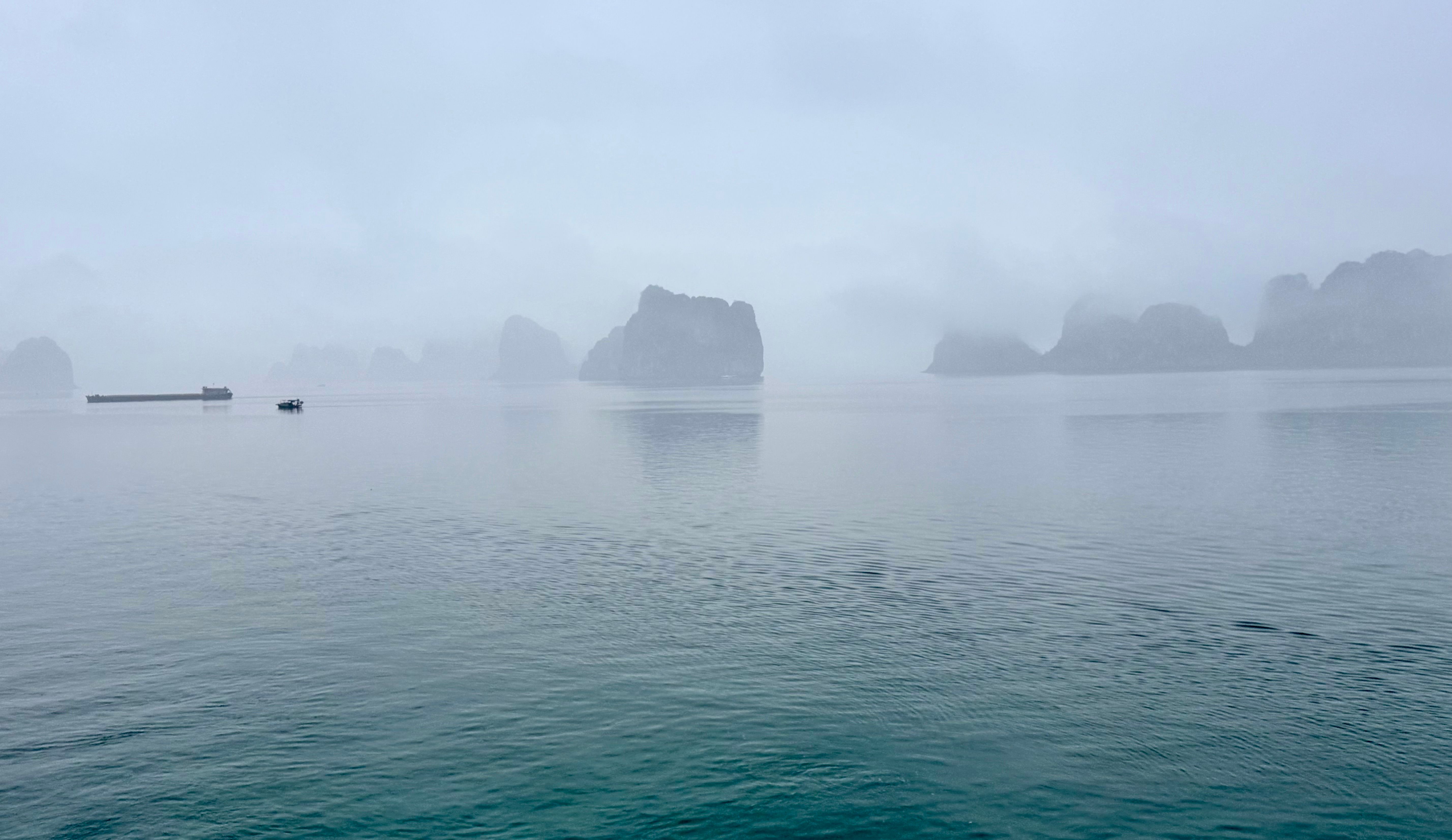 Serene misty morning view of Ha Long Bay, Vietnam, with rocky outcrops and calm waters.