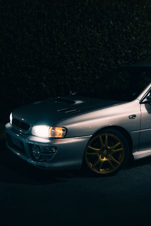 Free Silver sports car with golden wheels illuminated by headlights at night. Stock Photo