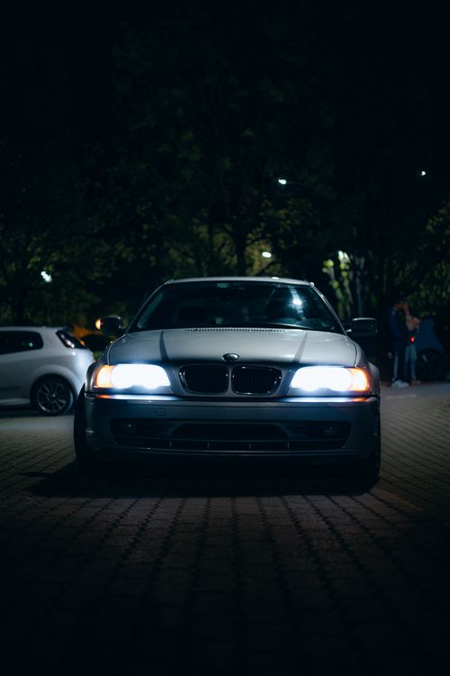 Free A car with headlights on, parked outdoors at night in a dimly lit area. Urban setting, moody atmosphere. Stock Photo