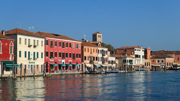 Brightly colored houses line the canal in Murano, Venice, Italy, reflecting in the water.