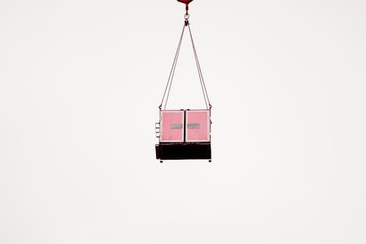 A pink cargo container suspended mid-air against a clear white sky, minimalist composition.