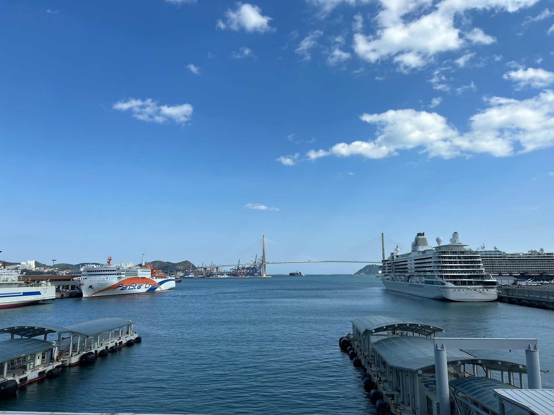 Sunny harbor with cruise ships, clear blue sky, and a distant bridge.