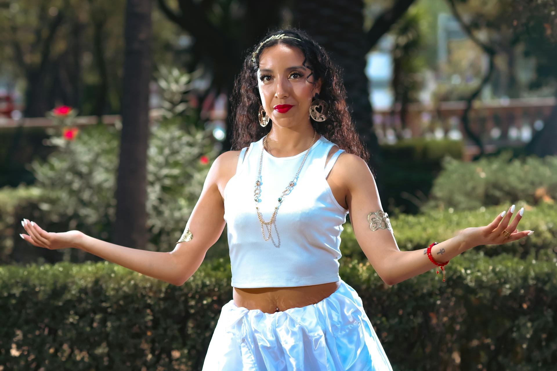 Confident bohemian woman poses in white attire with ethnic jewelry in a lush outdoor setting in Mexico City.
