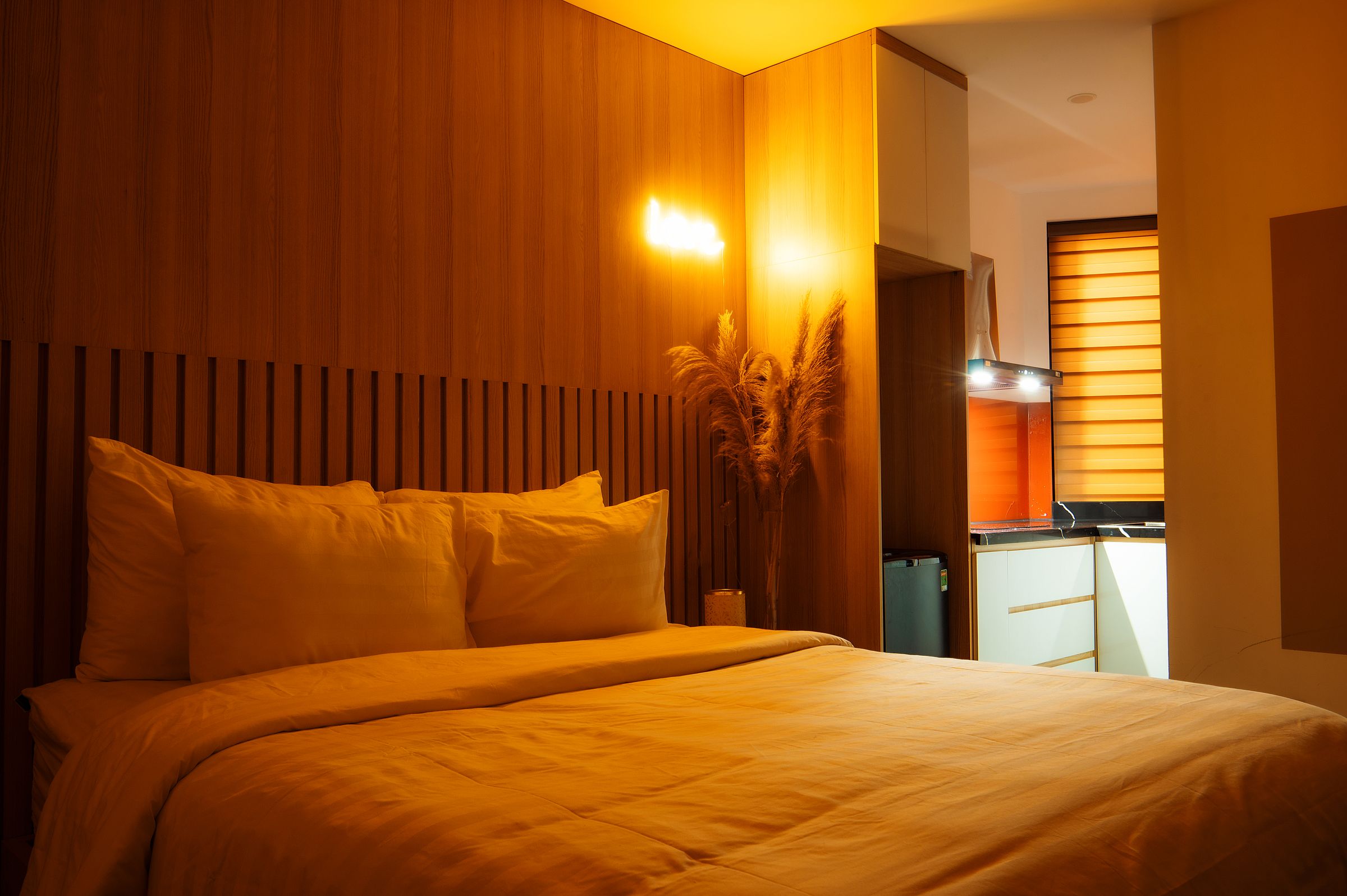 Wide bedroom with timber wall paneling, a glowing bedside pendant and a second low lamp near the bed