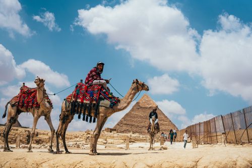 Free Camel riders in vibrant attire near the Great Pyramid of Giza under a clear blue sky. Stock Photo