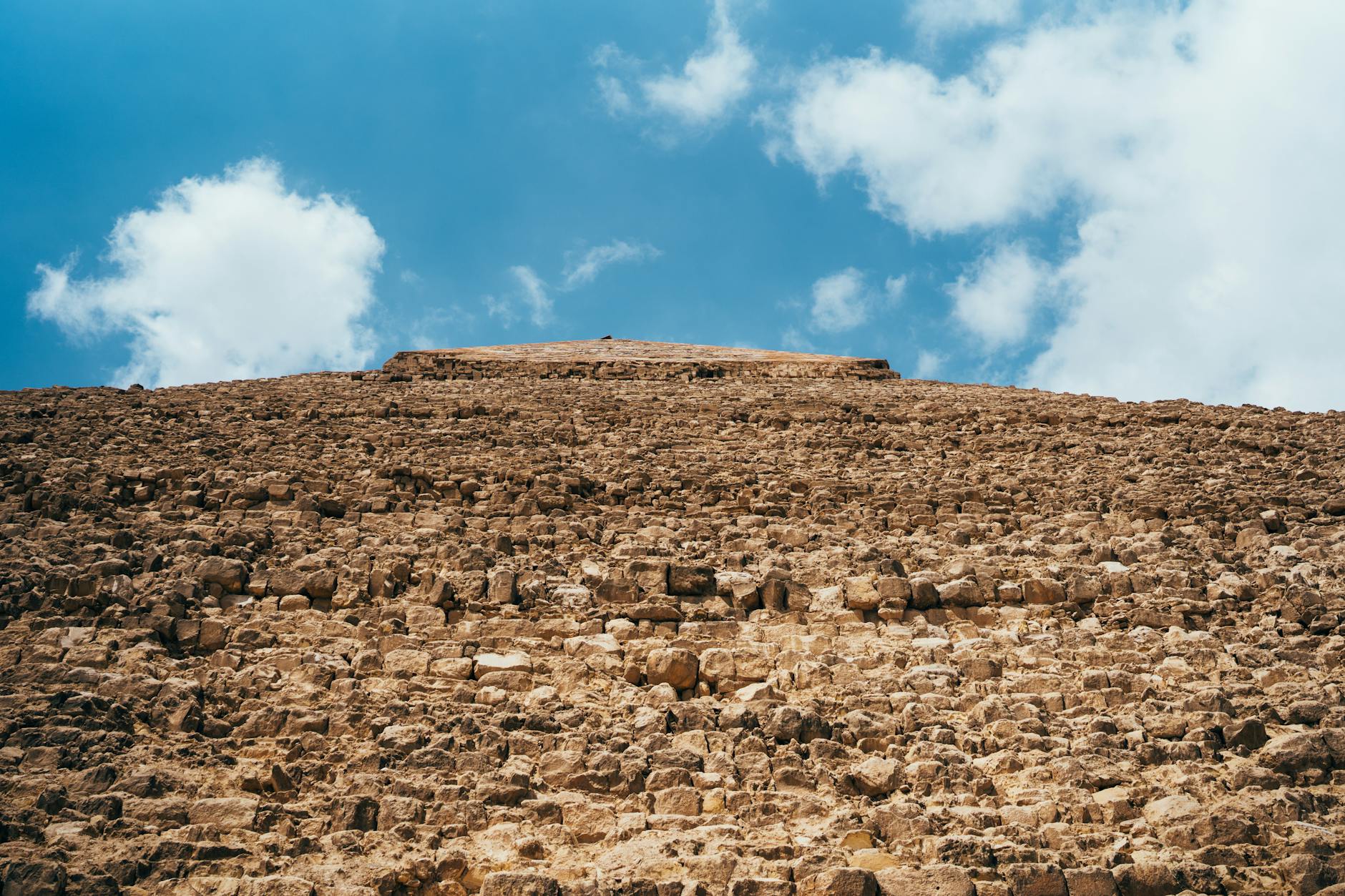 Low angle view of a pyramid's stone structure with clouds in the sky.