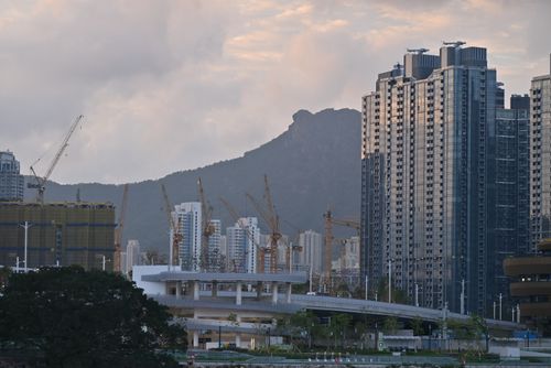 Free High-rise buildings and cranes against a mountain backdrop under a cloudy sky, showcasing urban growth. Stock Photo