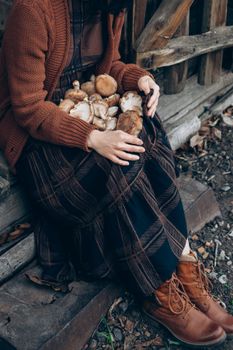 A woman sitting outdoors on a wooden step holding freshly picked mushrooms in autumn.
