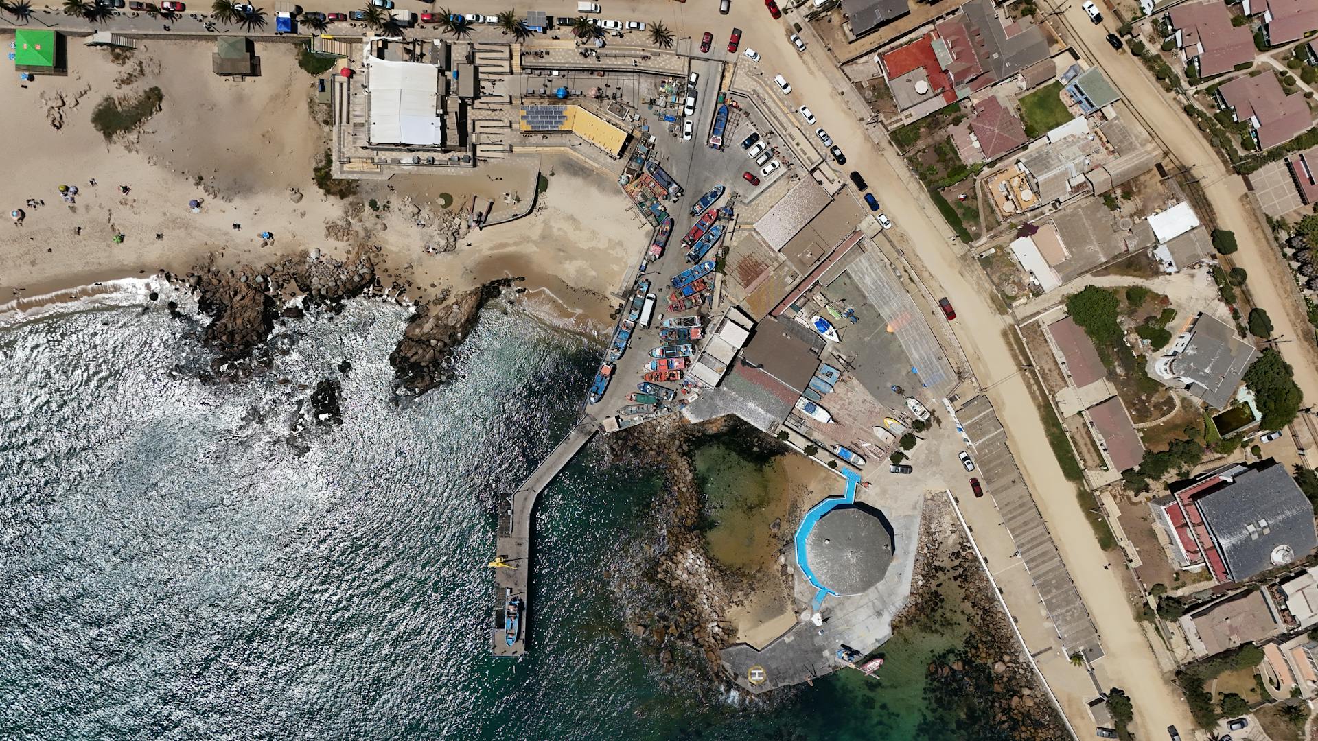 Aerial shot of a Chilean coastal village with beach, boats, and buildings.