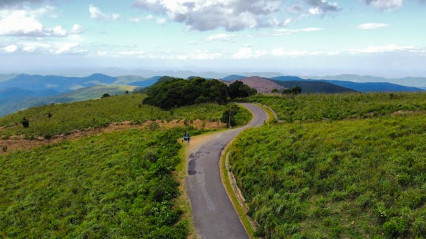 Aerial view of a winding road through verdant hills and distant mountains.