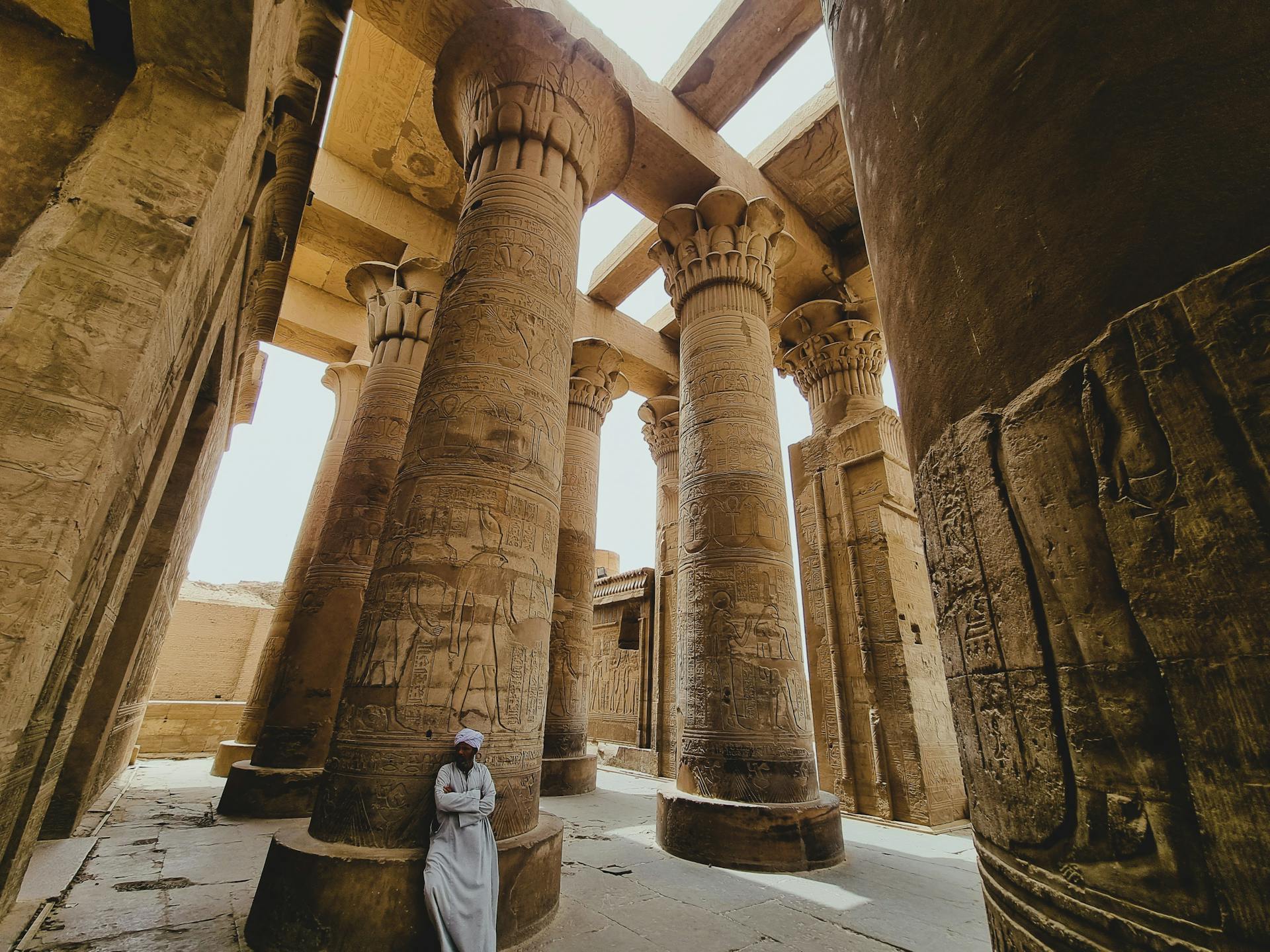 Explore the grandeur of ancient Egyptian temple columns with detailed hieroglyphs and a serene figure in traditional attire.