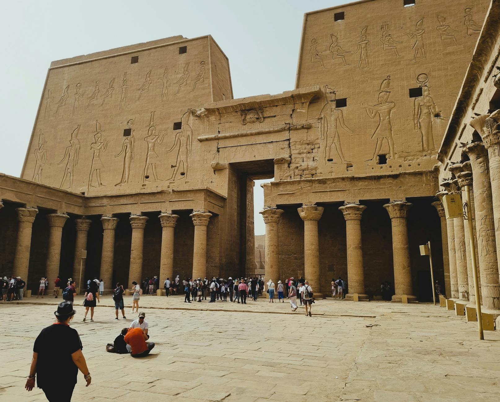 The towering carved first pylon and columned forecourt of the Temple of Horus at Edfu, with visitors below