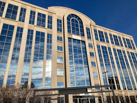 A modern office building with a striking glass facade reflecting a blue sky.