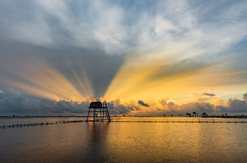 Free Breathtaking view of a coastal sunrise with dramatic rays and a silhouetted structure on water. Stock Photo