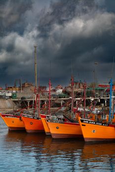 Vibrant orange fishing boats docked under dramatic skies in Mar del Plata, Argentina.