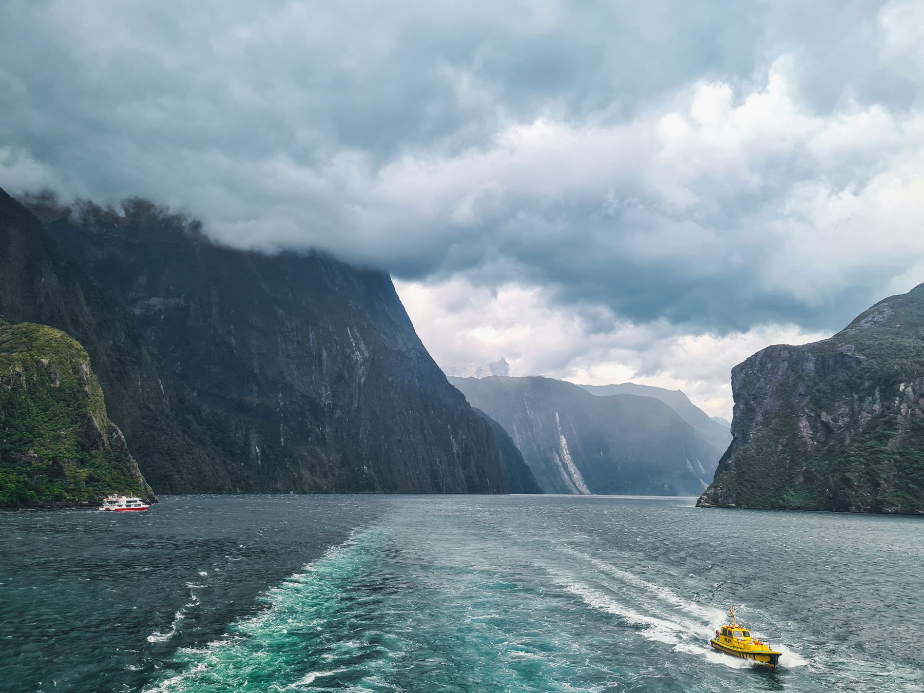 Boats beneath steep mountains in Milford Sound, New Zealand