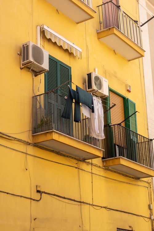 Free A vibrant yellow building facade featuring balconies with clothes hanging out to dry. Stock Photo