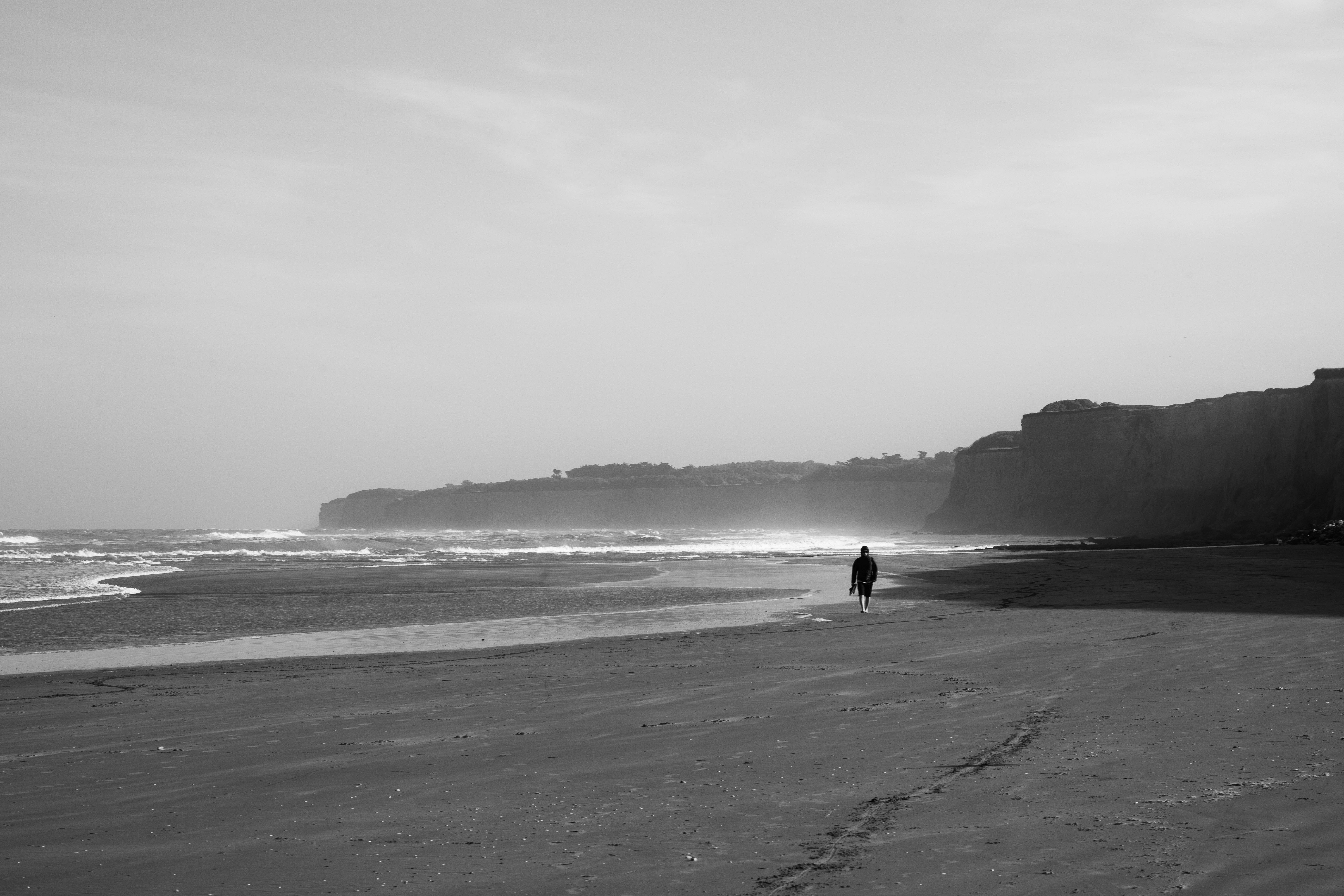 A solitary figure walks along a tranquil beach in Mar del Plata, Argentina, under overcast skies.