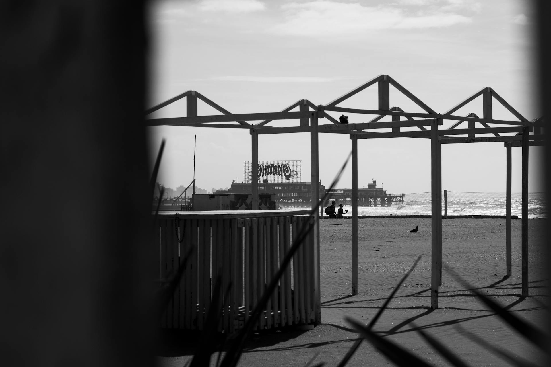 Artistic black and white photo of beach scene with pier and geometric structure.