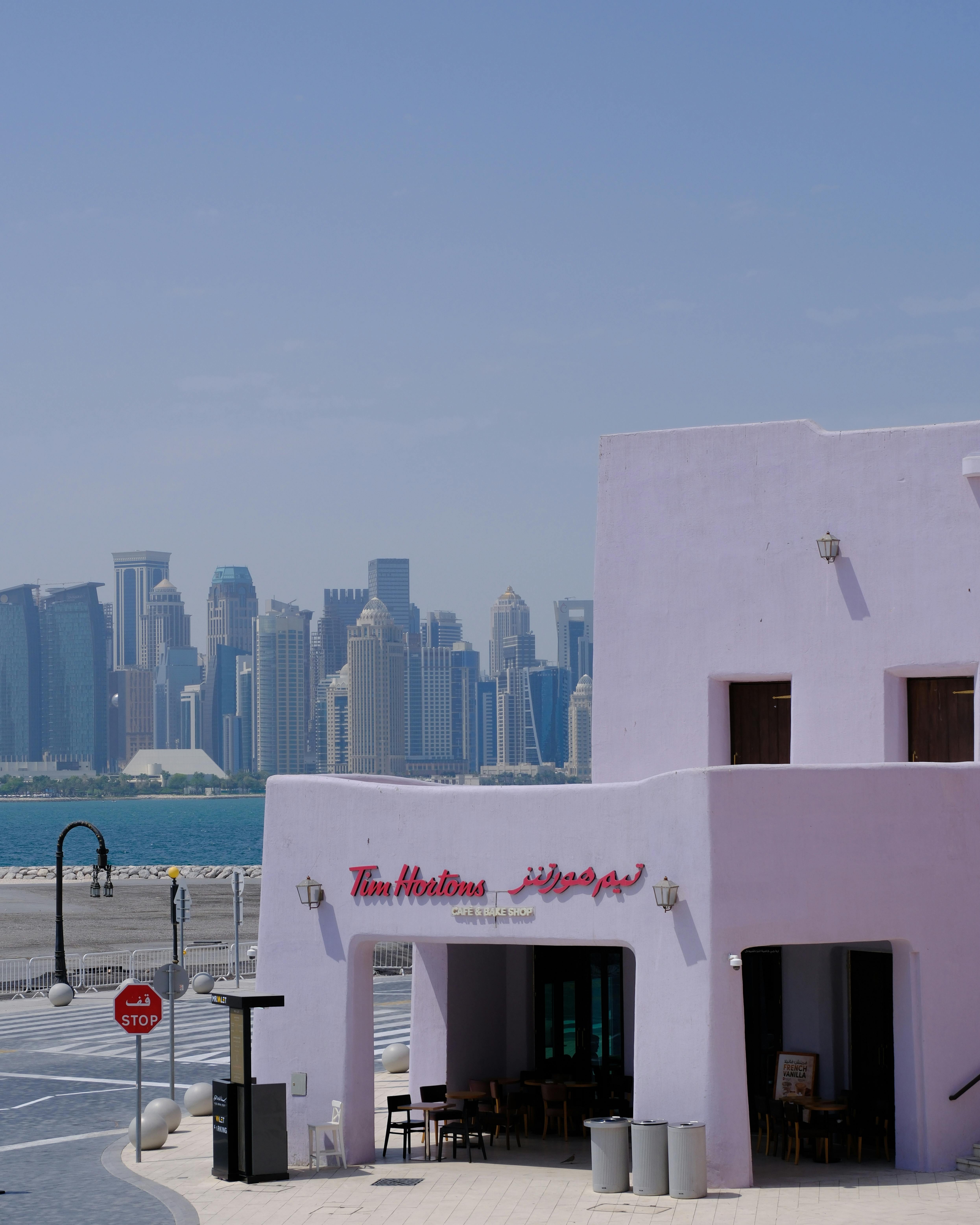 A Tim Hortons cafe facade set against the stunning Doha skyline under a clear blue sky.
