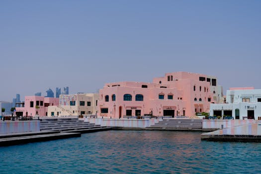 Pastel-colored buildings along a waterfront in Doha, Qatar with a city skyline backdrop.