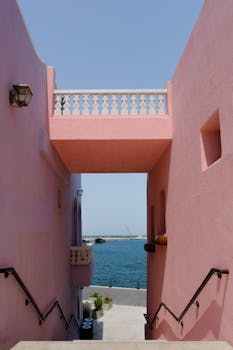 Pink buildings frame a serene sea view under a clear blue sky.