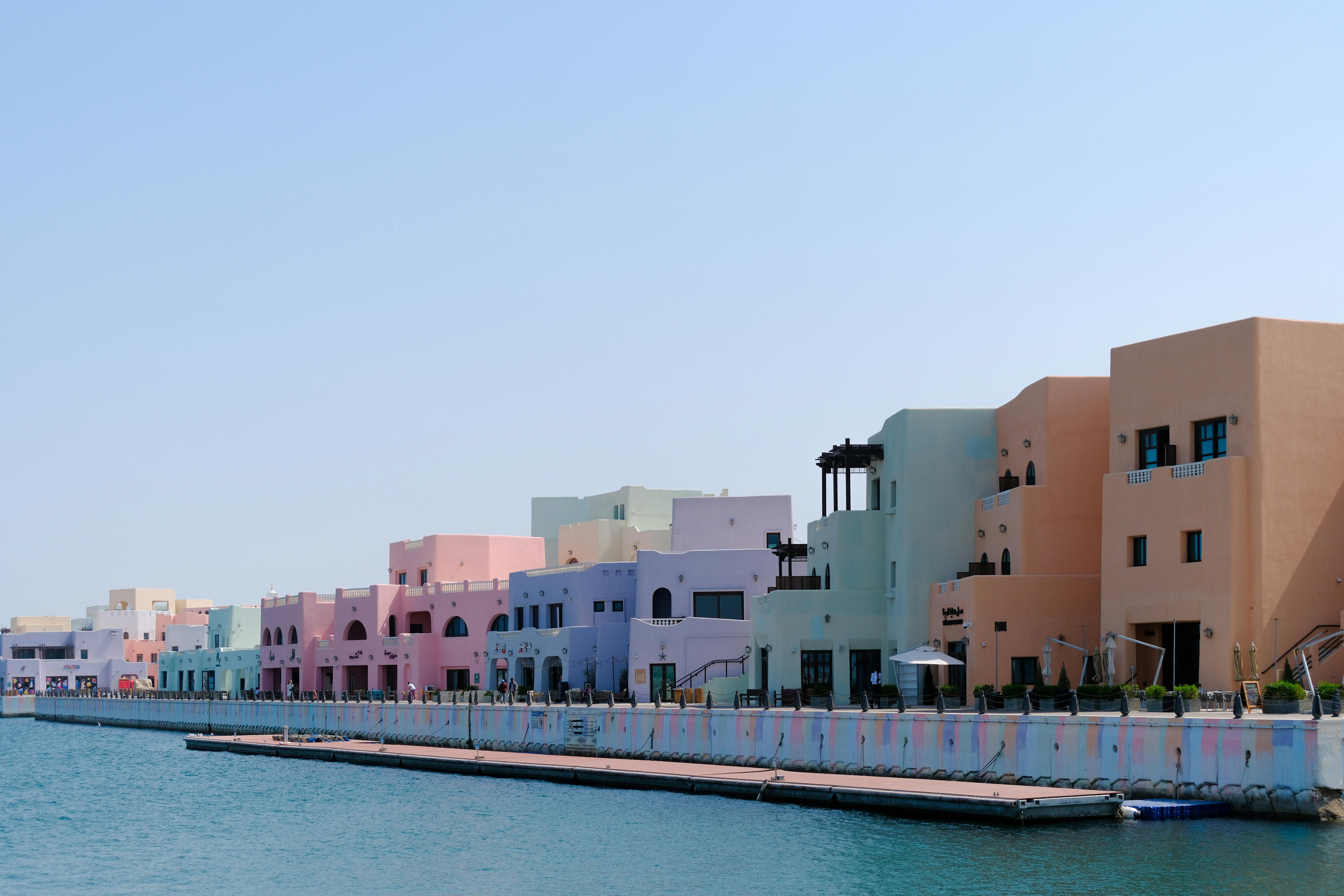 Vibrant pastel buildings line a waterfront under a bright blue sky, creating a scenic view.
