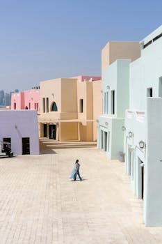 Woman walking among colorful pastel buildings on a sunny day.