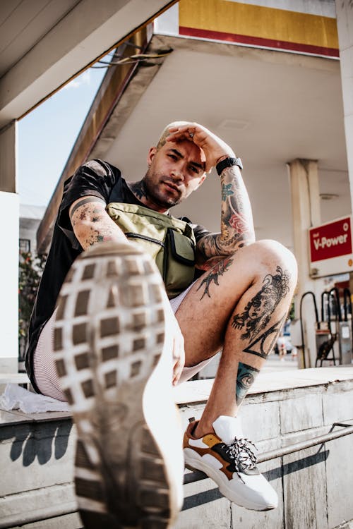 Low Angle Shot Of A Man With Tattoos Sitting With His Hand On His Forehead