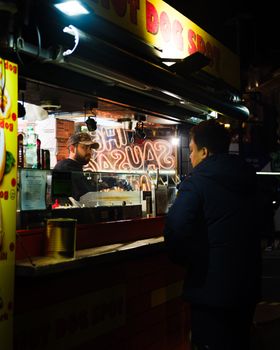 Candid shot of a street food vendor at a hot dog stand in downtown London at night.