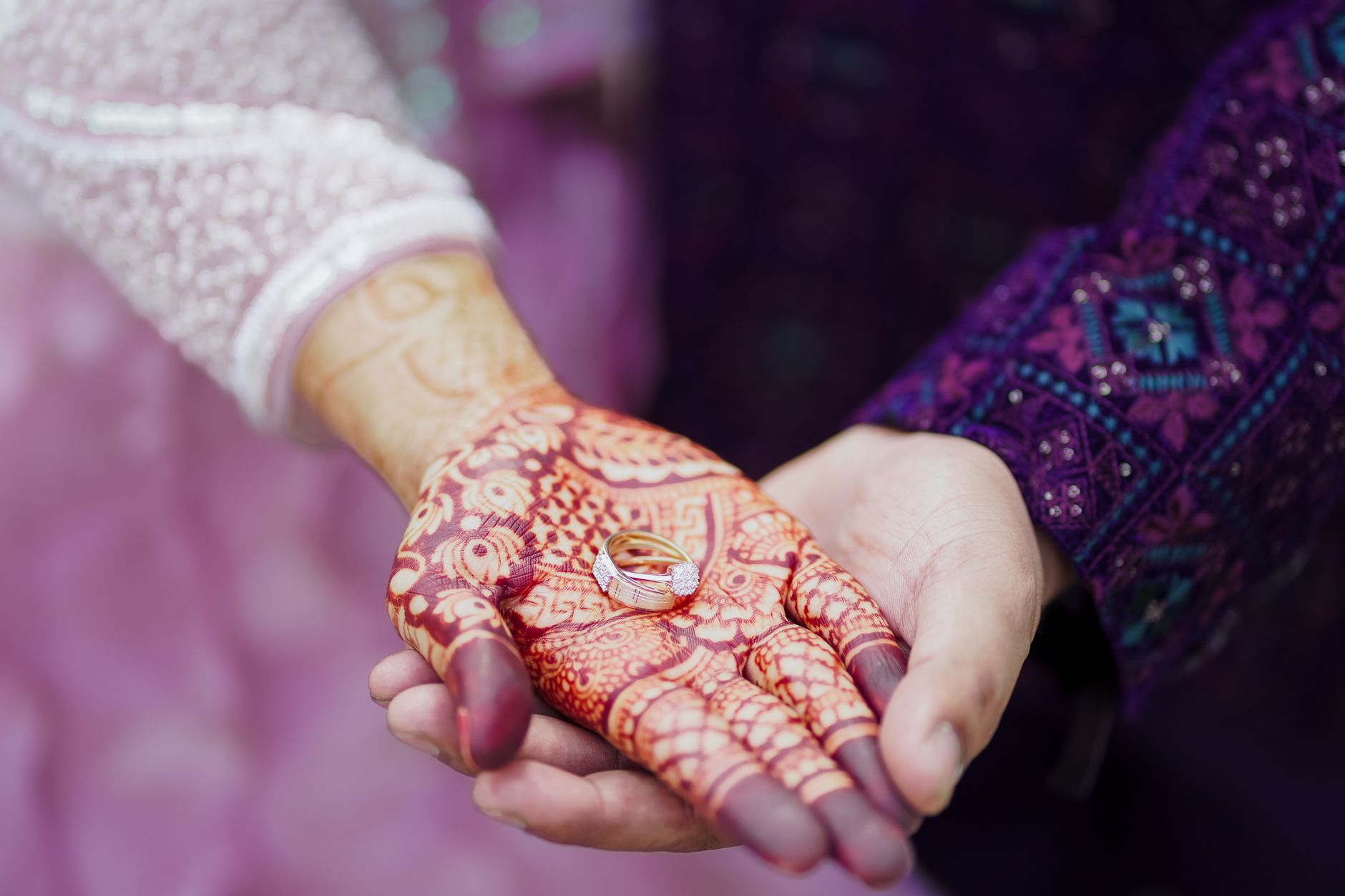 Close-up of a couple's hands, adorned with Mehndi and wedding rings, showcasing love and tradition.