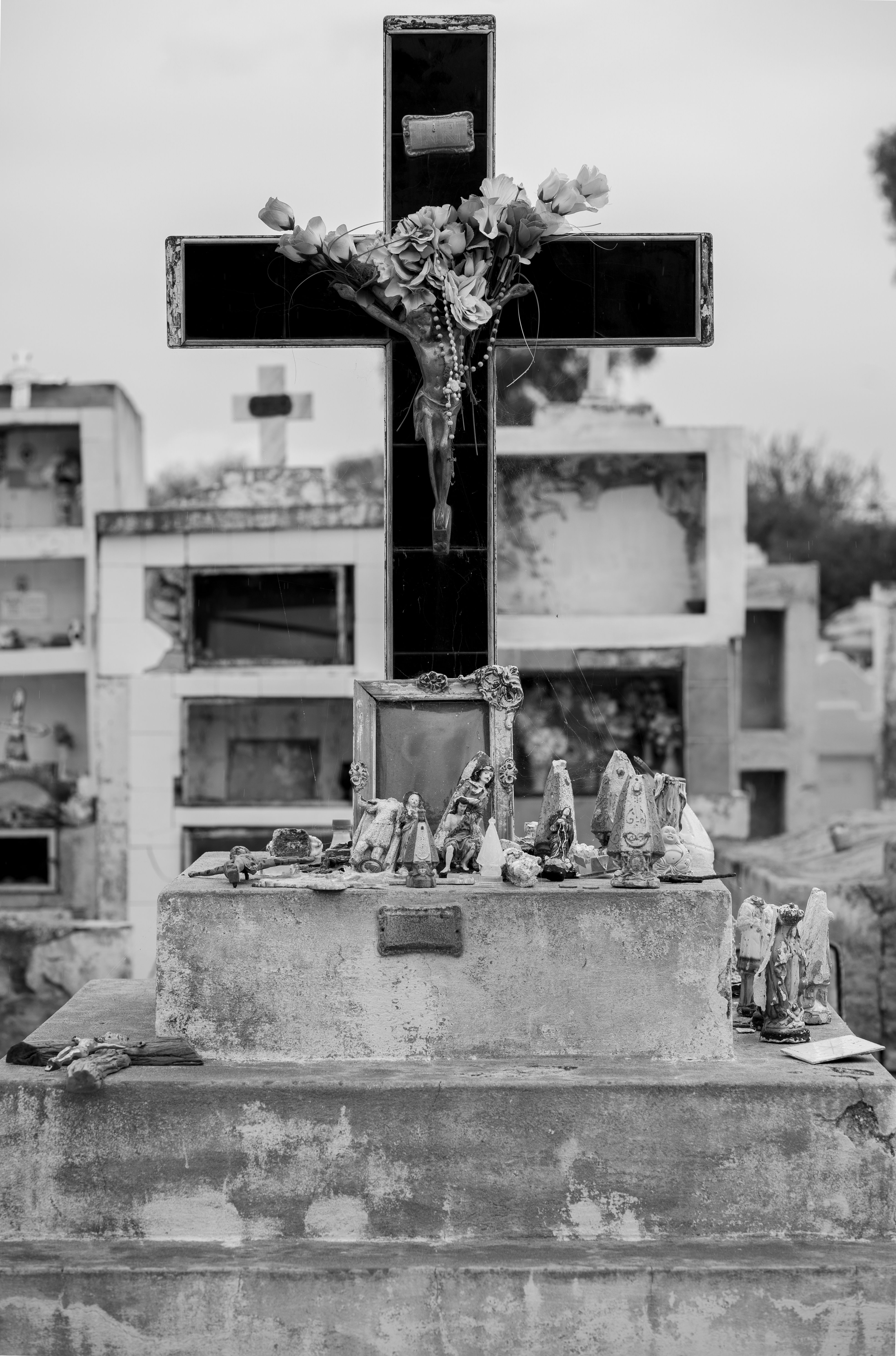 Black cross adorned with flowers and religious icons in a Córdoba cemetery.