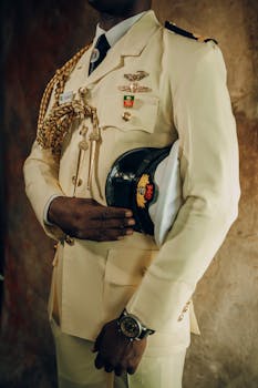 Close-up of a military officer in a cream formal uniform holding a cap, showcasing medals and insignia.