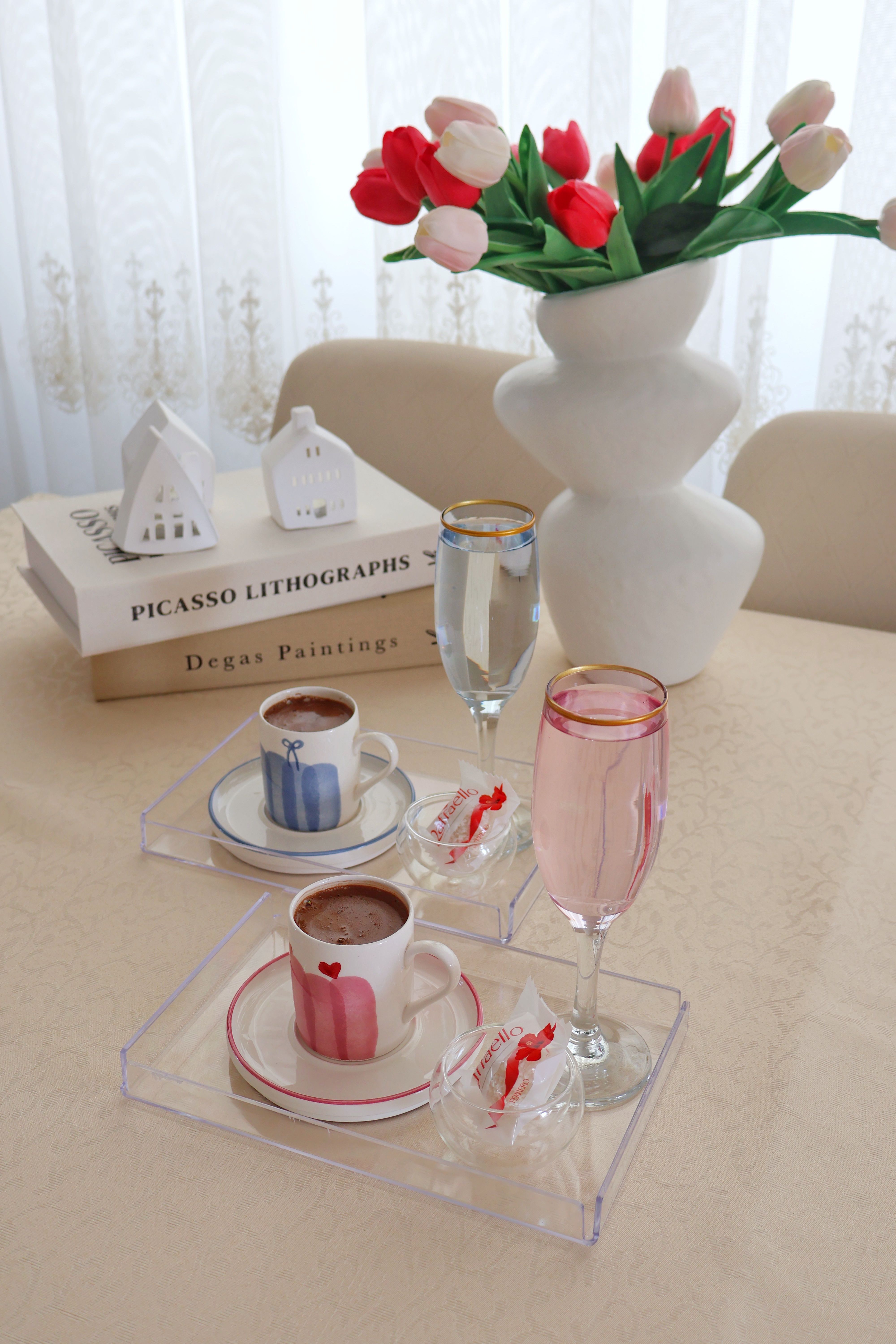 Stylish coffee setup with tulips, books, and clear trays for a luxurious indoor ambiance.