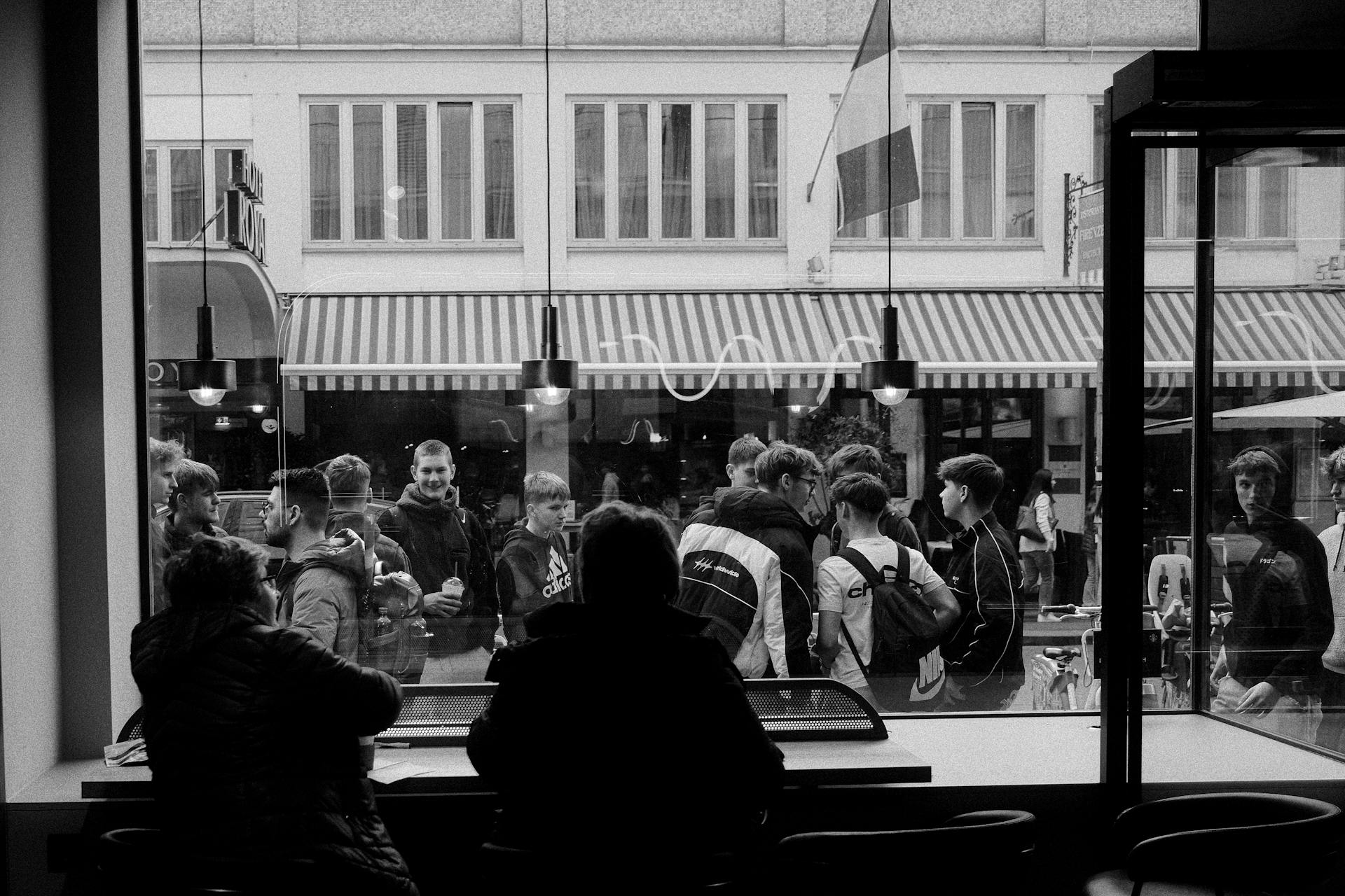 Monochrome view of street crowd from inside a café, capturing urban social dynamics.