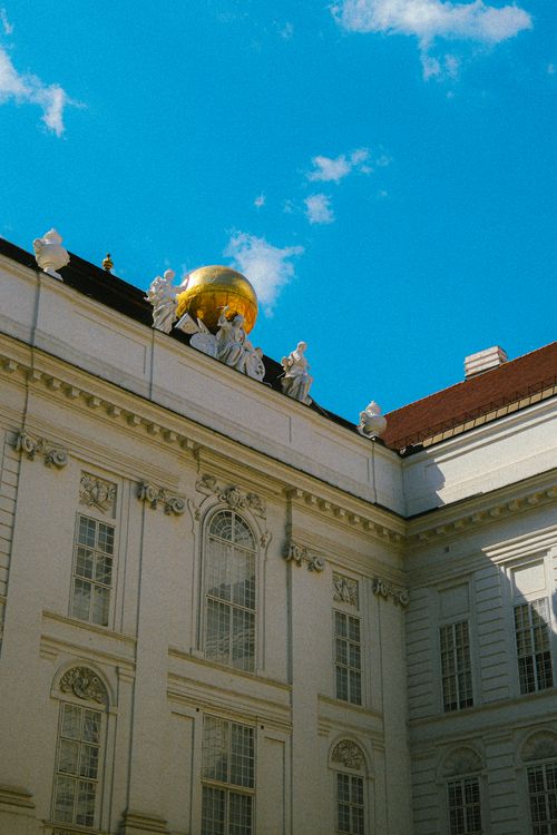Free Elegant Baroque building adorned with a golden globe sculpture against a clear blue sky. Stock Photo