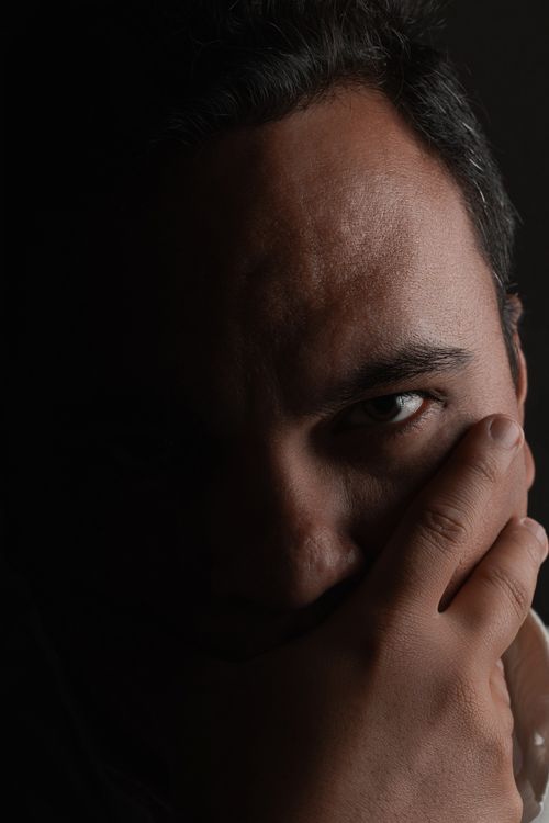 Free Dramatic close-up portrait of a man partially in shadow, covering mouth with hand. Stock Photo