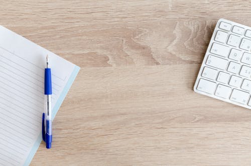 Blue Retractable Pen on Top of Notebook Near Magic Keyboard