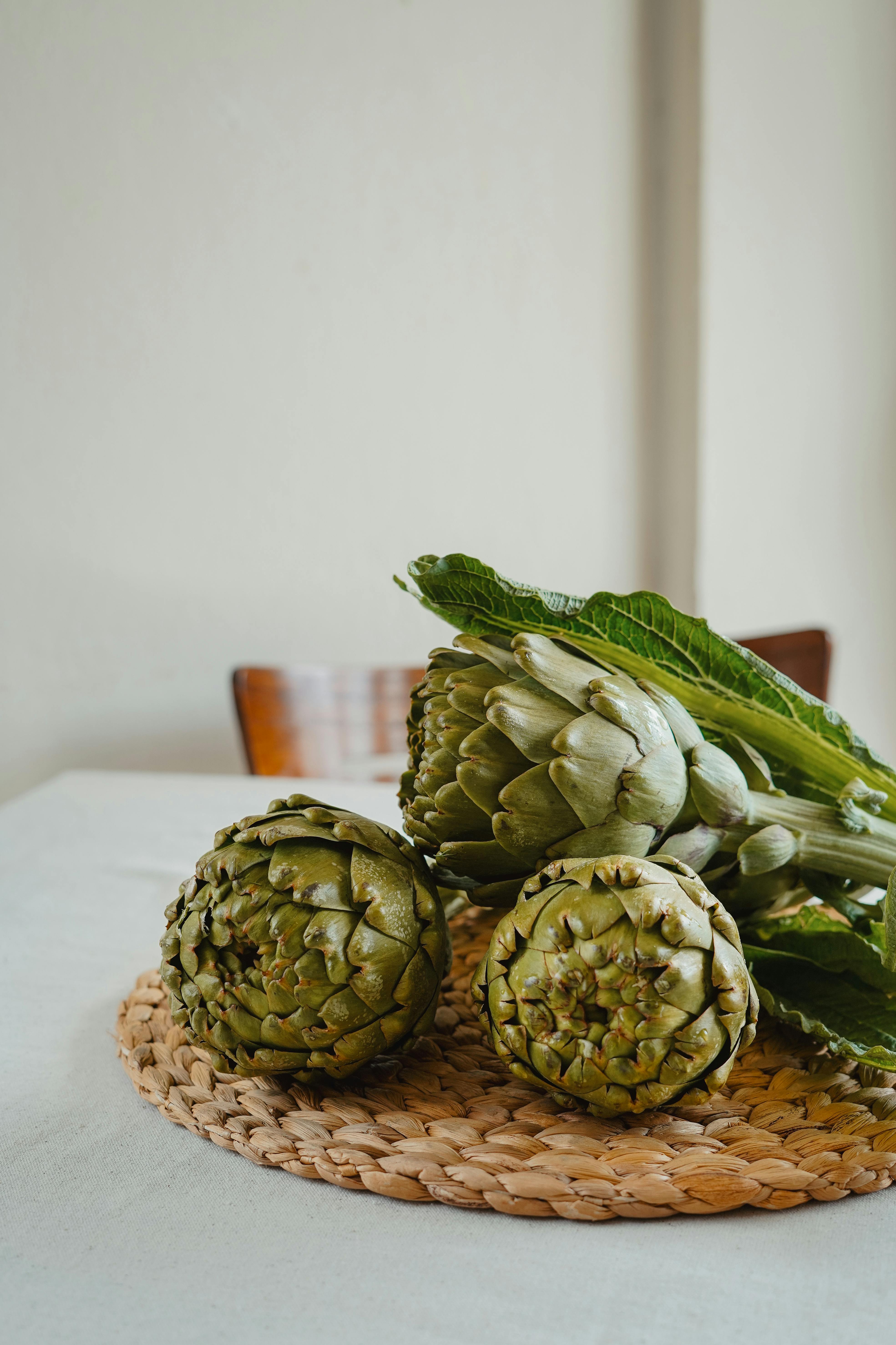 A still life composition featuring fresh artichokes on a woven table mat indoors.