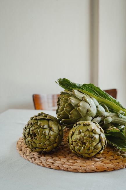 A still life composition featuring fresh artichokes on a woven table mat indoors.