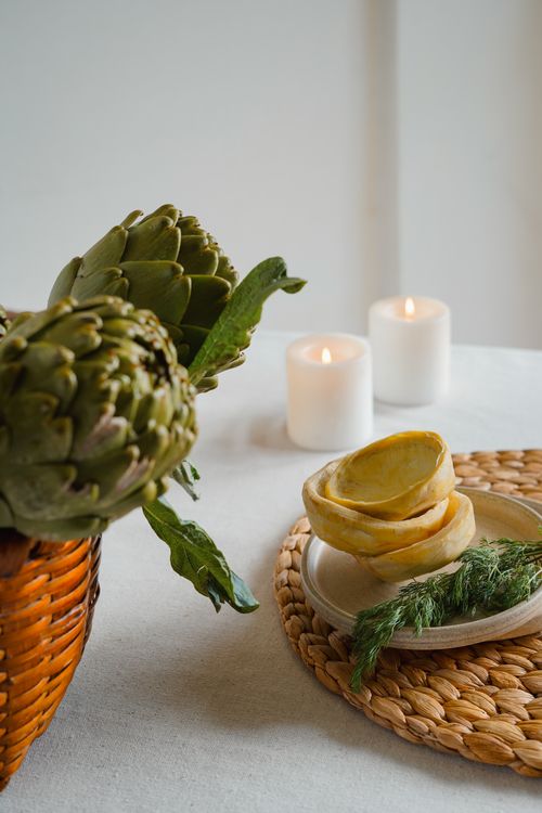 Free Still life of fresh artichokes with candles and dill on woven mat. Stock Photo