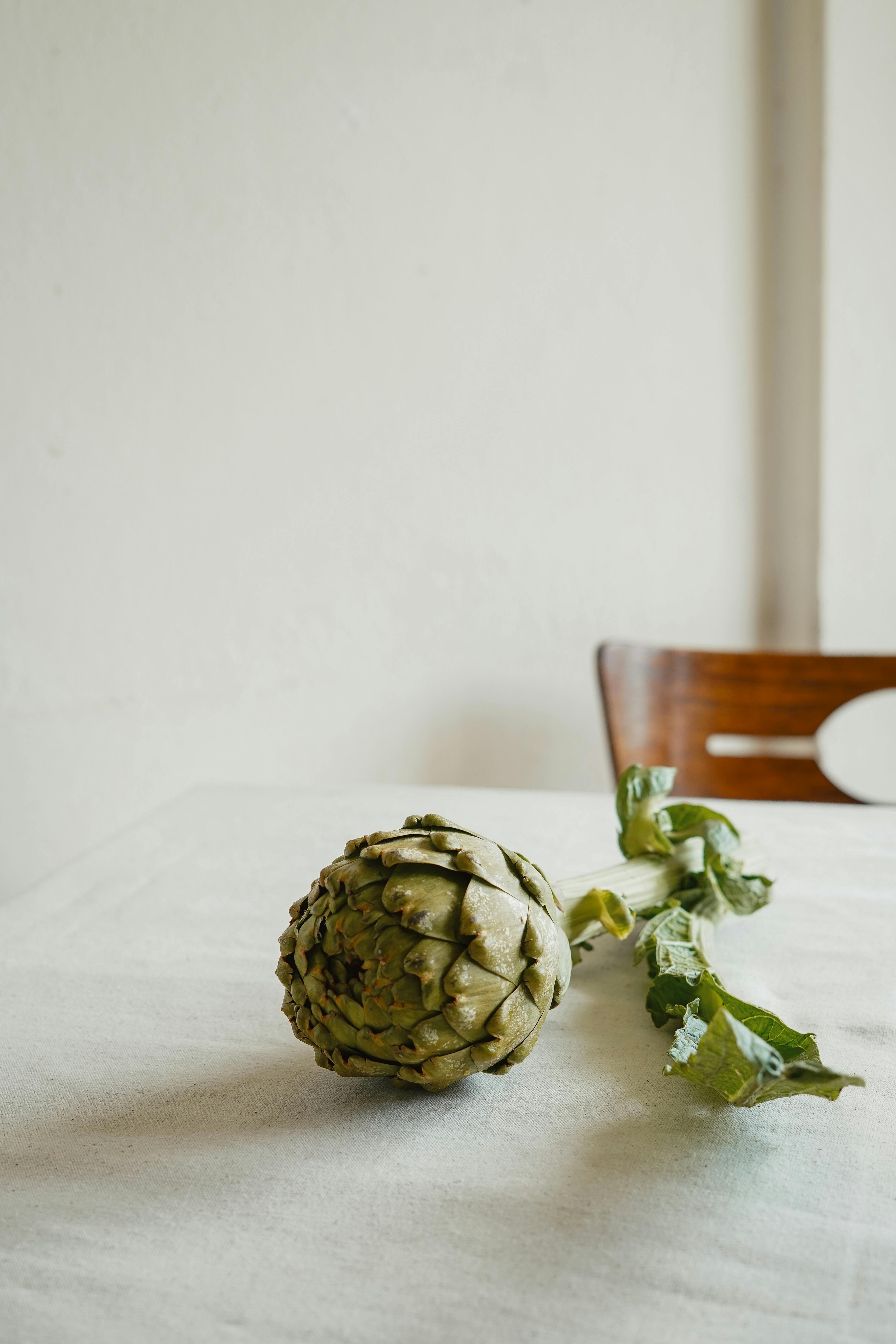 A single artichoke rests on a wooden table, captured in a minimalist style with a neutral background.