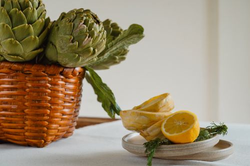 Free Fresh artichokes in a basket with sliced lemons on a ceramic plate, creating a rustic kitchen scene. Stock Photo