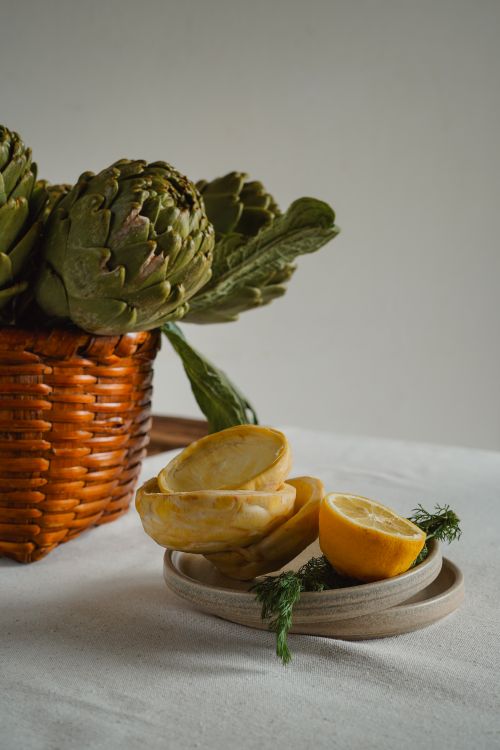 Free Artistic composition of artichokes in a basket with sliced lemons on a plate. Stock Photo