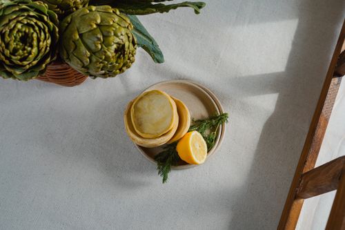 Free Artichokes and lemon on a ceramic plate with a rustic background, perfect for culinary themes. Stock Photo