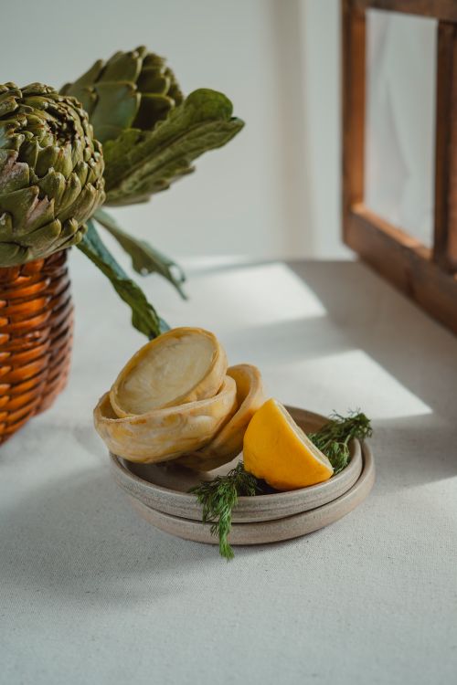 Free A minimalist still life featuring artichokes and a lemon slice in warm daylight. Stock Photo